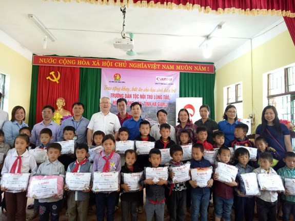 Ông Minoru Niimura-Tổng giám đốc Công ty TNHH Canon Việt Nam (hàng sau cùng, thứ 4 từ trái sang) cùng các đại biểu tặng quà và chụp ảnh lưu niệm với học sinh nhà trường.